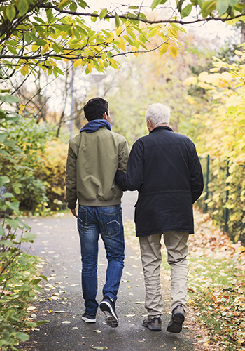 En ung och en gammal man håller armkrok på promenad.