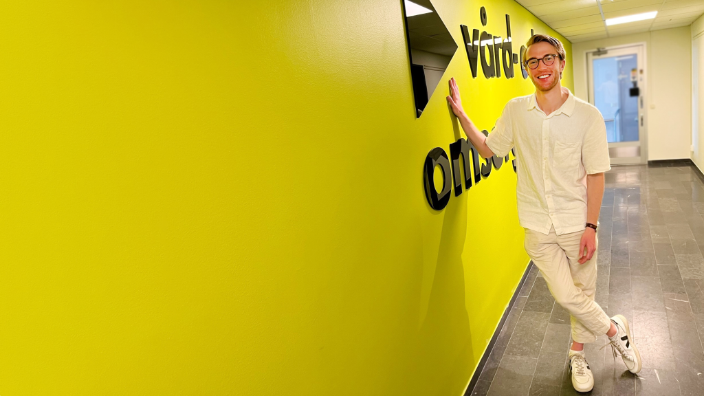 Fredrik Strelert står lutad mot en gröngul vägg med Vård- och omsorgsanalys logotyp.