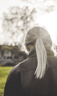 En ung kvinna sedd bakifrån står med sänkt huvud.