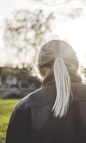 En ung kvinna sedd bakifrån står med sänkt huvud.