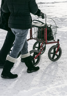 Två personer går tillsammans vid en rollator i snö.