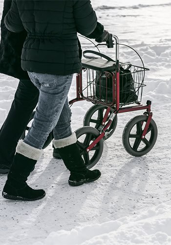 Två personer går tillsammans vid en rollator i snö.