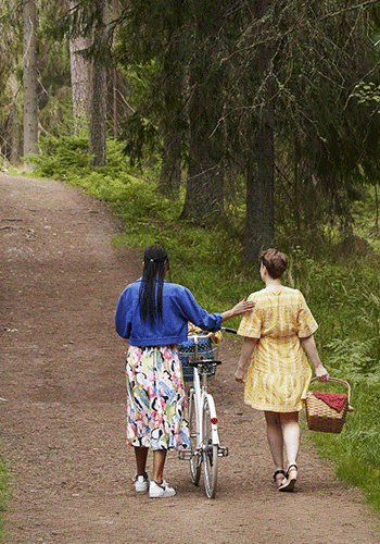 Två kvinnor går på en skogsväg med cykel och picknickkorg.
